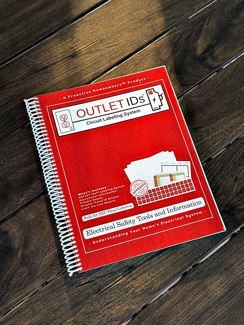 The red spiral-bound OUTLET IDs Circuit Labeling System book at an angle on a wooden table